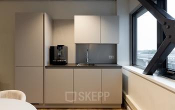 Modern kitchenette in office at Vanadiumweg 11, Amersfoort Isselt, featuring a coffee machine, sleek cabinets, and a view from the window, perfect for office space rental.