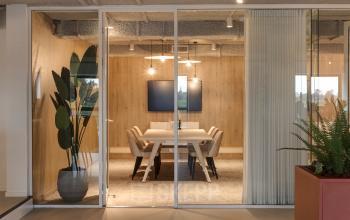 Modern conference room with wooden accents at Vanadiumweg 11, Amersfoort Isselt, suitable for office space rental. Features glass walls, a large table, sleek chairs, and decorative plants.