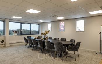 Spacious, modern conference room at Vanadiumweg 11, Amersfoort Isselt, featuring a large table and plush chairs. Ideal for office space rental with ample natural light from large windows.