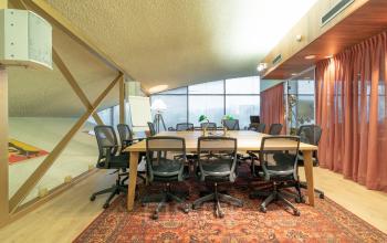 Conference room with a large wooden table, multiple ergonomic chairs, and a vintage-style carpet located at Prof. W.H. Keesomlaan 12, Amstelveen. Office space rental available.