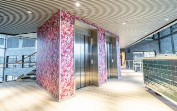 Colorful and modern elevator area with floral walls and wooden flooring in the office space located at Prof. W.H. Keesomlaan 12, Amstelveen.