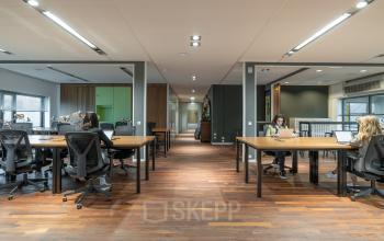 Modern office space with wooden flooring and large desks at Prof. W.H. Keesomlaan 12, Amstelveen. People working on laptops at shared desks. Ideal for office space rental.