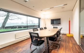 Modern conference room at Prof. W.H. Keesomlaan 12 in Amstelveen, featuring a long table, chairs, TV, and large window.