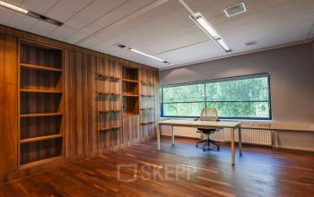 Spacious office to rent at Prof. W.H. Keesomlaan 12, Amstelveen, featuring a single desk, chair, large window, and wooden shelving units along one wall.