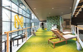 Modern office interior at Prof. W.H. Keesomlaan 12, Amstelveen, featuring artificial grass flooring, lounge chairs, and floor-to-ceiling windows.