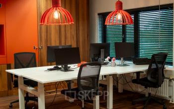Modern office space for rent at Prof. W.H. Keesomlaan 12, Amstelveen featuring a shared workspace with desks, chairs, computers, and vibrant red hanging lights.