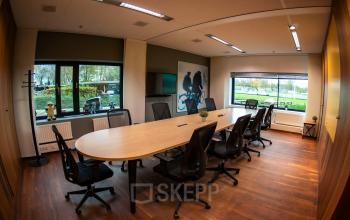 Conference room with large oval table, black chairs, and windows overlooking greenery at Prof. W.H. Keesomlaan 12, Amstelveen. Ideal office space rental for meetings.