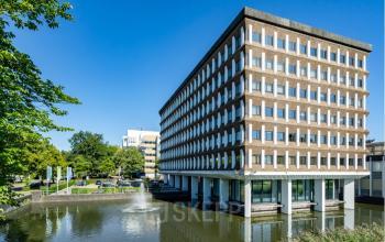 Exterior view of the office building at Professor E.M. Meijerslaan 1, Amstelveen, surrounded by greenery and adjacent to a fountain pond. Ideal location for office space rental.