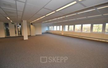 Spacious unfurnished office space with large windows at Stroombaan 4, Amstelveen, available for rent. Neutral-toned carpet and overhead lighting with ample natural light.