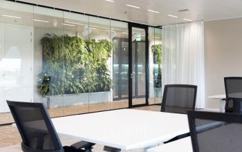 Modern office space with white desks and ergonomic chairs at Amsterdam Amstel Business Park, featuring a green plant wall. Ideal for office space rental.
