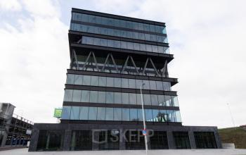 Exterior view of a modern office building with large glass windows, located at Joan Muyskenweg 137 in Amsterdam Amstel Business Park, ideal for office space rental.