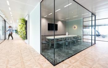 Modern office space for rent in Amsterdam Amstel Business Park, featuring a glass-walled conference room and a person walking down the hall.