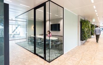 Modern office space at Amsterdam Amstel Business Park, featuring glass-walled conference room with a person working at a desk. Ideal for office space rental.