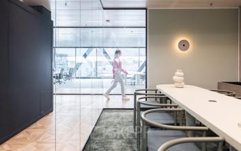 Modern office space with glass walls at Amsterdam Amstel Business Park. A person walks by the work area, showcasing a sleek environment ideal for office space rental.