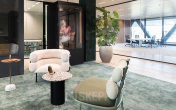 Modern office space with stylish seating area and a meeting room available for rent in Amsterdam Amstel Business Park. A person is visible in the background engaged in work.