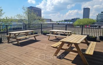 Wooden picnic benches on a rooftop terrace at Willem Fenengastraat 2, Amsterdam Amstel Business Park with a view of city buildings.