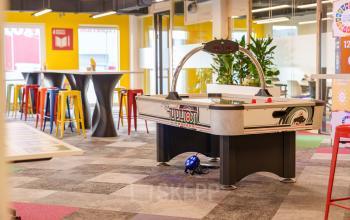 Colorful office space with air hockey table, high tables with stools, and large windows, located at Willem Fenengastraat 2, Amsterdam Amstel Business Park, ideal for office space rental.