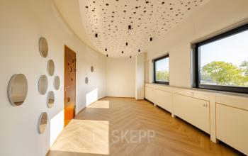 Bright office interior with decorative ceiling and circular wall mirrors in the Amsterdam Amstel Business Park, available for office space rental. Large windows offer natural light and views of greenery.