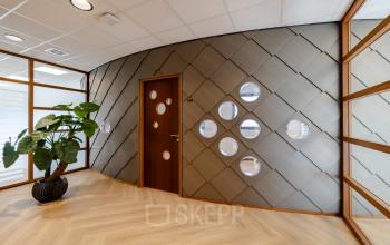 Modern office space with sleek wooden flooring and a unique geometric wall design, located in Joan Muyskenweg 82, Amsterdam Amstel Business Park. Ideal for office space rental, featuring stylish interiors and natural light.