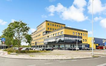 A modern, yellow and gray four-story office building in Amsterdam Amstel Business Park, featuring ample parking. Perfect for those seeking office space rental.