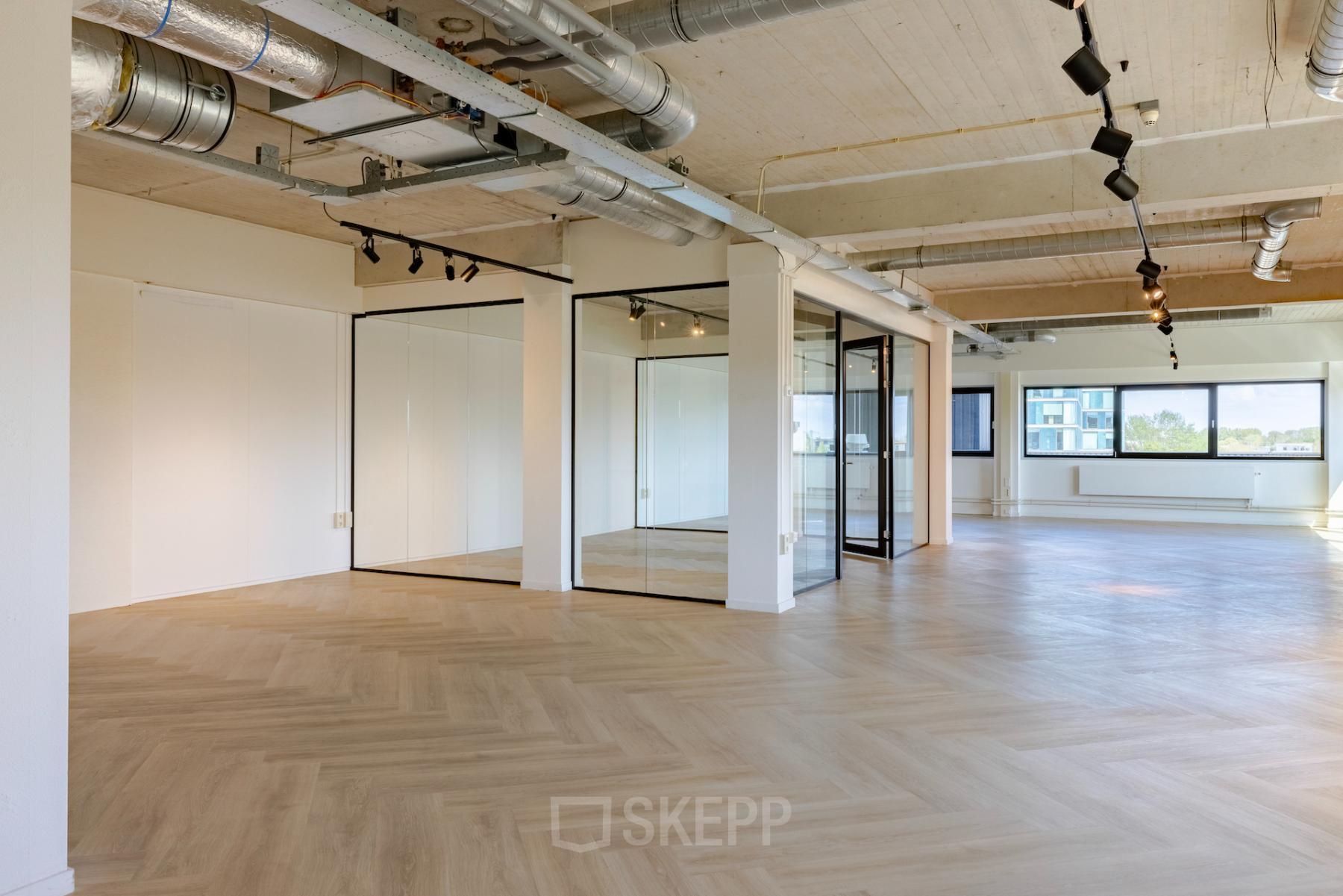 Spacious and modern office space to rent at Joan Muyskenweg 40 - 148, Amsterdam Amstel Business Park, featuring large windows, exposed ceilings, and glass-walled meeting rooms.