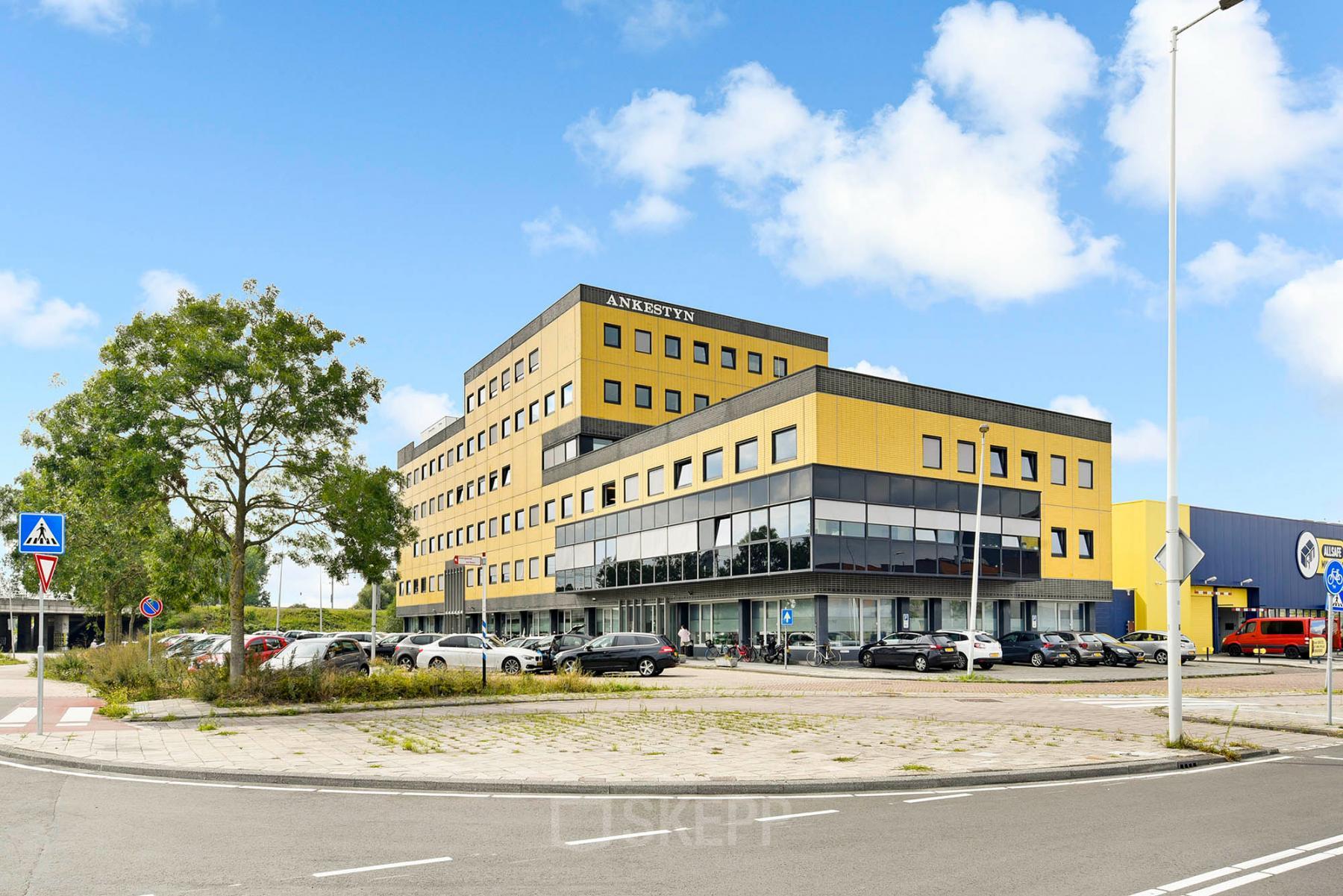 A modern, yellow and gray four-story office building in Amsterdam Amstel Business Park, featuring ample parking. Perfect for those seeking office space rental.