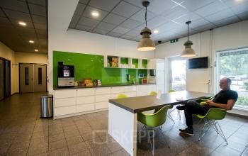 Modern pantry area at office space rental at Joop Geesinkweg 901-999, Amsterdam Amstel Business Park, with a person seated and drinking coffee.