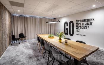 Clean modern workspace at Joan Muyskenweg 22 in Amsterdam Amstel Business Park featuring a large wooden conference table, chairs, potted plants, and motivational wall art.