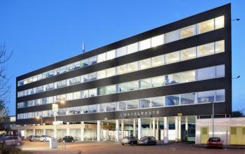 Exterior of the office building located at Joan Muyskenweg 22, in Amsterdam Amstel Business Park, Amsterdam, featuring multiple floors with large windows and cars parked in front. Office space rental available.