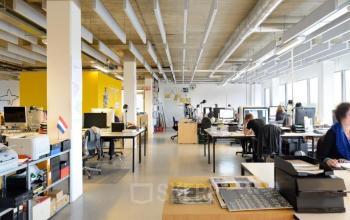 Open-floor office space rental at Joan Muyskenweg 22 in Amsterdam Amstel Business Park with several people working at desks, bright lighting, and industrial design.
