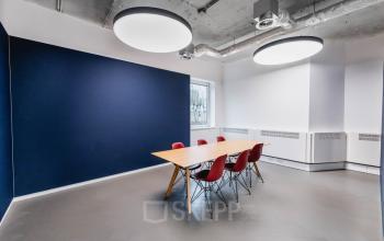 Office space with a large wooden table and red chairs, under modern circular ceiling lights at H.J.E. Wenckebachweg 90-108, Amsterdam Amstel Business Park.