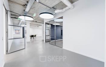 Modern office space with glass doors, grey flooring, and large circular lighting fixtures at H.J.E. Wenckebachweg 90-108 in Amsterdam Amstel Business Park.