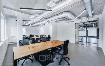 Modern office space with industrial-style ceiling, large windows, and multiple black desks and chairs at H.J.E. Wenckebachweg 90-108, Amsterdam Amstel Business Park.