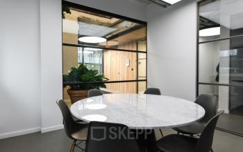A furnished meeting room with a round marble table and six chairs in a modern office available for rent at Amsterdam Amstel Business Park.