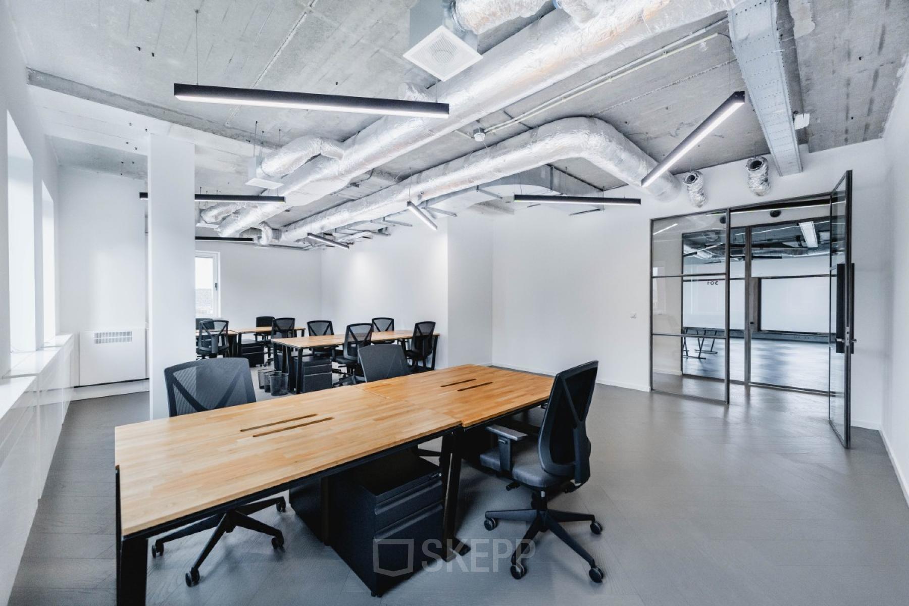 Modern office space with industrial-style ceiling, large windows, and multiple black desks and chairs at H.J.E. Wenckebachweg 90-108, Amsterdam Amstel Business Park.