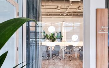 Modern office space rental at Joop Geesinkweg 601, Amsterdam Amstel Business Park, with a sleek glass door, white chairs, and a wooden floor.