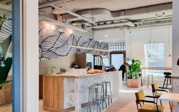 Modern and cozy interior of an office space rental in Joop Geesinkweg 601, Amsterdam Amstel Business Park, featuring a communal kitchen area with bar stools and chairs.