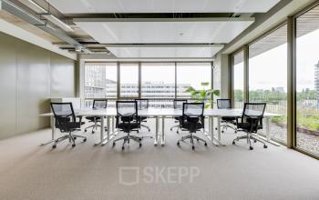 Bright office space with large windows and several desks and chairs, offering a professional workspace for rent in Amsterdam Amstel.