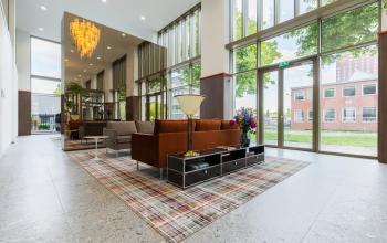 Bright and modern office space with floor-to-ceiling windows, contemporary furnishings, and a stylish chandelier, located at Willem Fenengastraat 16 in Amsterdam Amstel. Ideal for office space rental.