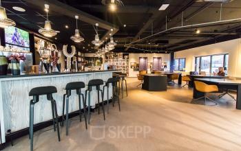 Spacious and modern office space rental at Prins Bernhardplein 200, Amsterdam Amstel, featuring stylish furnishings and a welcoming atmosphere with people collaborating at tables.
