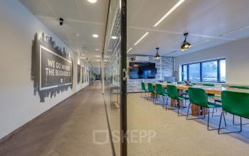 Spacious office space at Prins Bernhardplein 200, Amsterdam Amstel, with a conference room featuring green chairs and a large table, ideal for meetings. Perfect for office space rental.