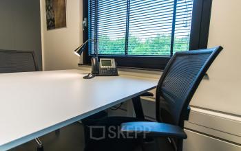 Modern office space rental at De Cuserstraat 93, Amsterdam Buitenveldert, featuring a spacious desk, chair, and phone.