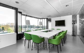 Modern office space rental at De Cuserstraat 93, Amsterdam Buitenveldert with a white conference table, green chairs, and a large window allowing for plenty of natural light.