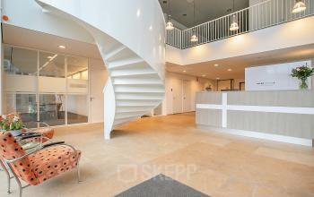 Modern office reception area with a sleek spiral staircase and contemporary furnishings at De Cuserstraat 91, ideal for office space rental in Amsterdam Buitenveldert.