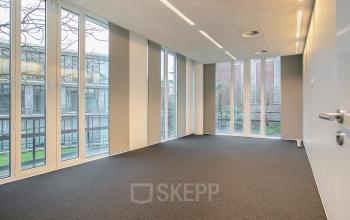 Spacious office for rent at De Cuserstraat 91 in Amsterdam Buitenveldert featuring large windows and neutral carpeting, ideal for any office space rental needs.