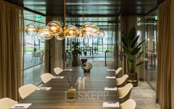 Spacious meeting room at Walborg 2A in Amsterdam Buitenveldert, ideal for office space rental, with a long table, modern lighting, and curtains framing glass walls.
