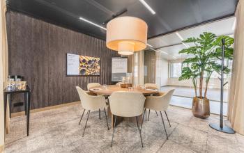 Modern office space for rent at Walborg 2A, Amsterdam Buitenveldert, featuring a meeting room with a round table, chairs, a large plant, and stylish lighting.