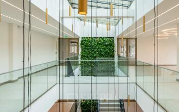 Spacious office area featuring a modern design with a glass atrium and hanging lights, located at Walborg 2A, Amsterdam Buitenveldert. Ideal for businesses seeking office space rental.