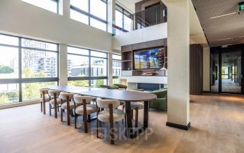 Bright workspace in Amsterdam Buitenveldert featuring a large table with chairs, overlooking an urban view through floor-to-ceiling windows, ideal for office space rental.