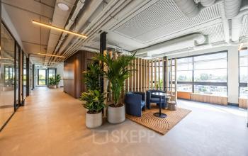 Modern office space at Zwaansvliet 1, Amsterdam Buitenveldert, featuring stylish furnishings, large windows, and plant decor. Ideal for office space rental.